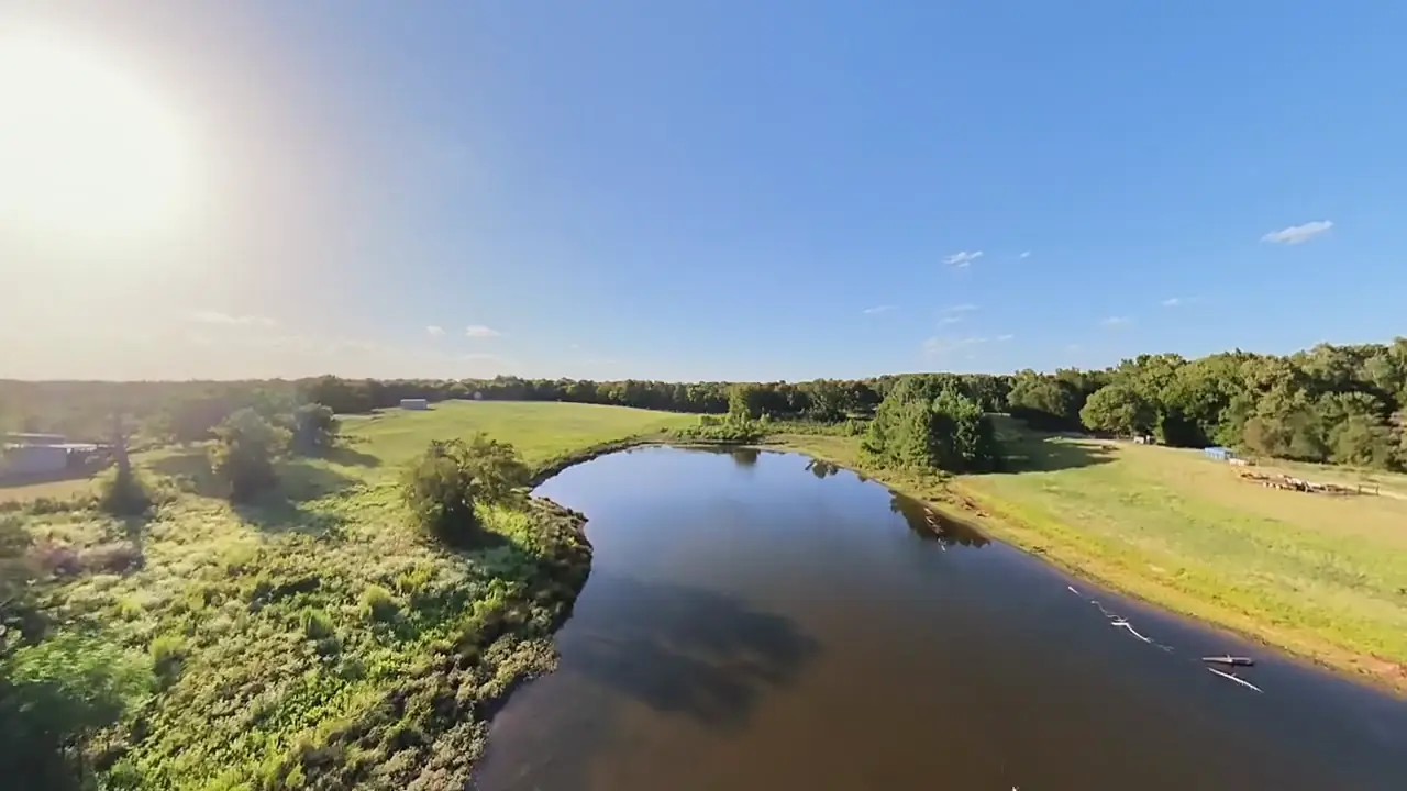 Drone view of a long curving pond with mowed pasture on one bank and woods on the other
